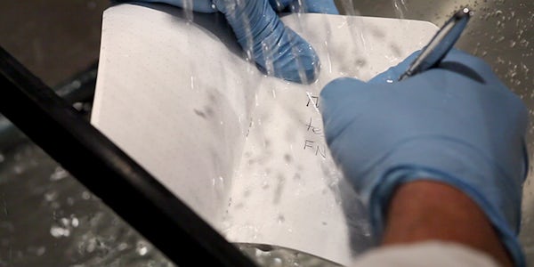 Person writing on waterproof notebook paper as water splashes on the paper.